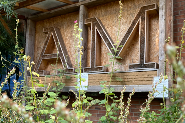 Die Buchstaben A und M von der Alten Mu aus Holz und Pflanzen im Vordergrund